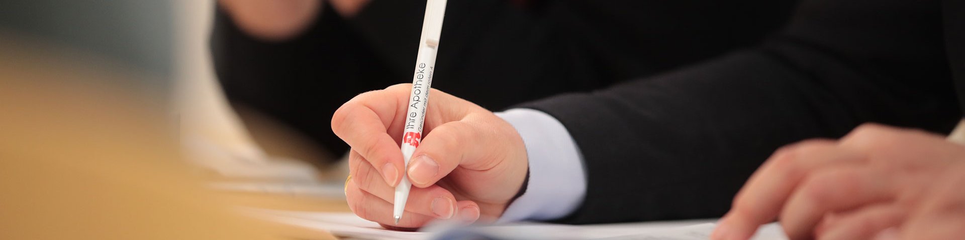 Meeting in der Bayerischen Landesapothekerkammer. Mitarbeiter sitzen an einem Tisch beieinander und es liegen Dokumente auf dem Tisch. Einer schreibt etwas.